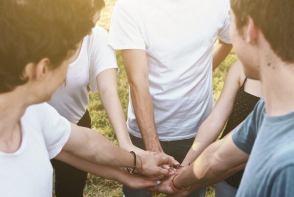 Group of men stacking hands outdoors, representing men's mental health and peer support