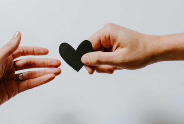 One hand passing a paper heart to another, representing the step down from PHP to IOP