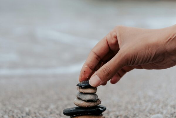 Hand stacking smooth stones on the shore, representing grounding and nervous system regulation in somatic experiencing therapy in Houston