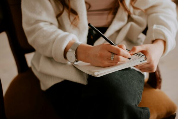 Person writing in a notebook during a therapy session, working on a treatment plan