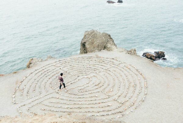 Person walking a sand labyrinth by the ocean, representing mindful, body based Somatic Experiencing