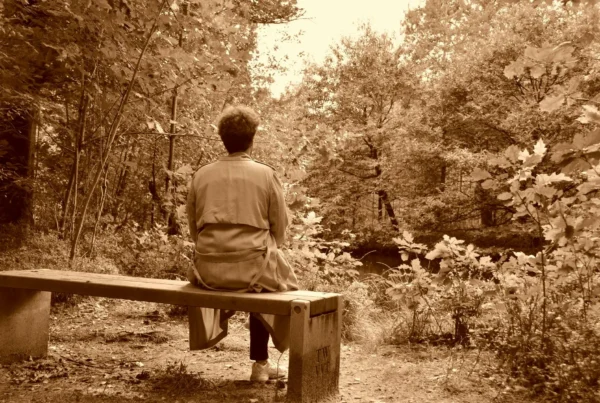 Person sitting on a wooden bench in a quiet forest practicing mindful acceptance and reflection