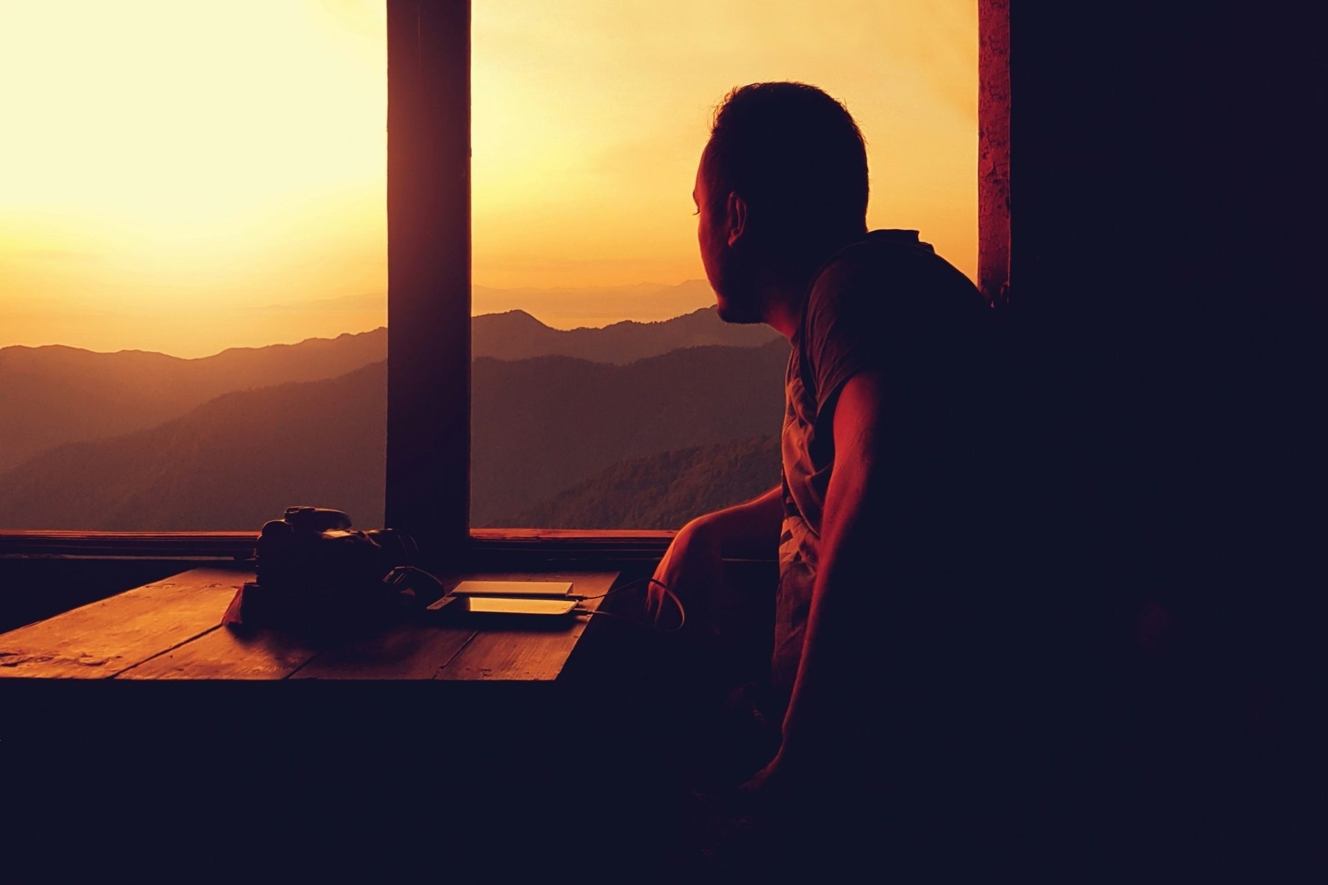 Man seated at a window as the sun sets over the hills, representing balance and rhythm in bipolar disorder treatment