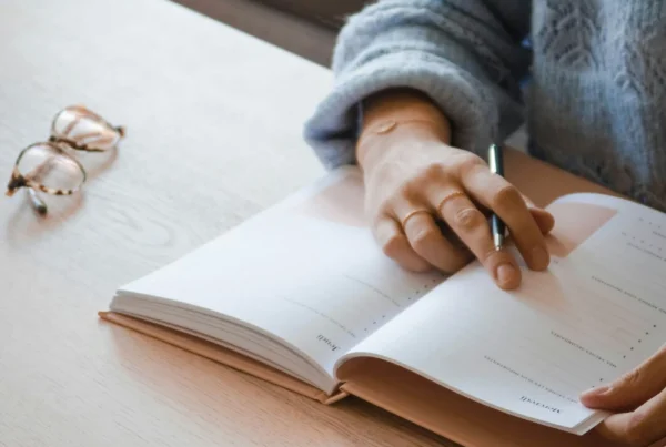 Hand writing in an open notebook beside reading glasses during treatment planning