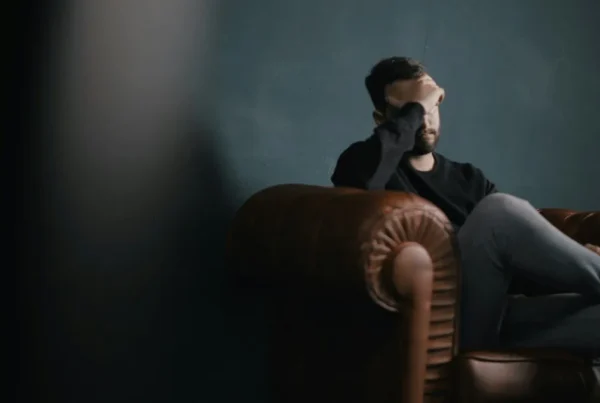 Man sitting in a leather armchair with his hand over his eyes, looking stressed, illustrating high-functioning anxiety