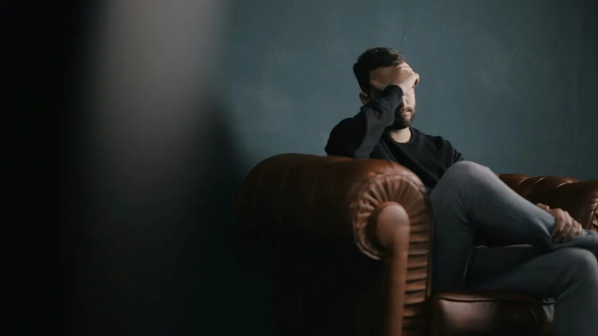 Man sitting in a leather armchair with his hand over his eyes, looking stressed, illustrating high-functioning anxiety