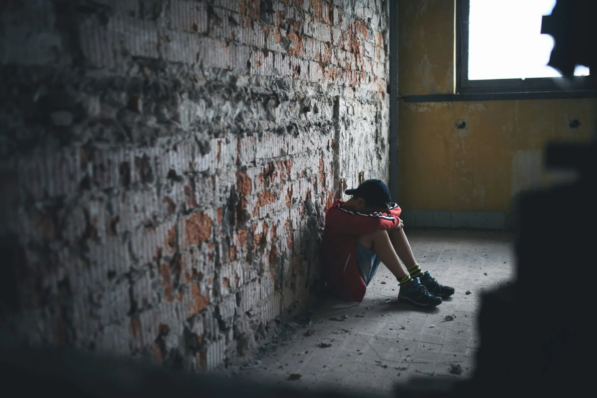 Person sitting alone against a brick wall, showing isolation during a substance use crisis, illustrating nitrous oxide misuse