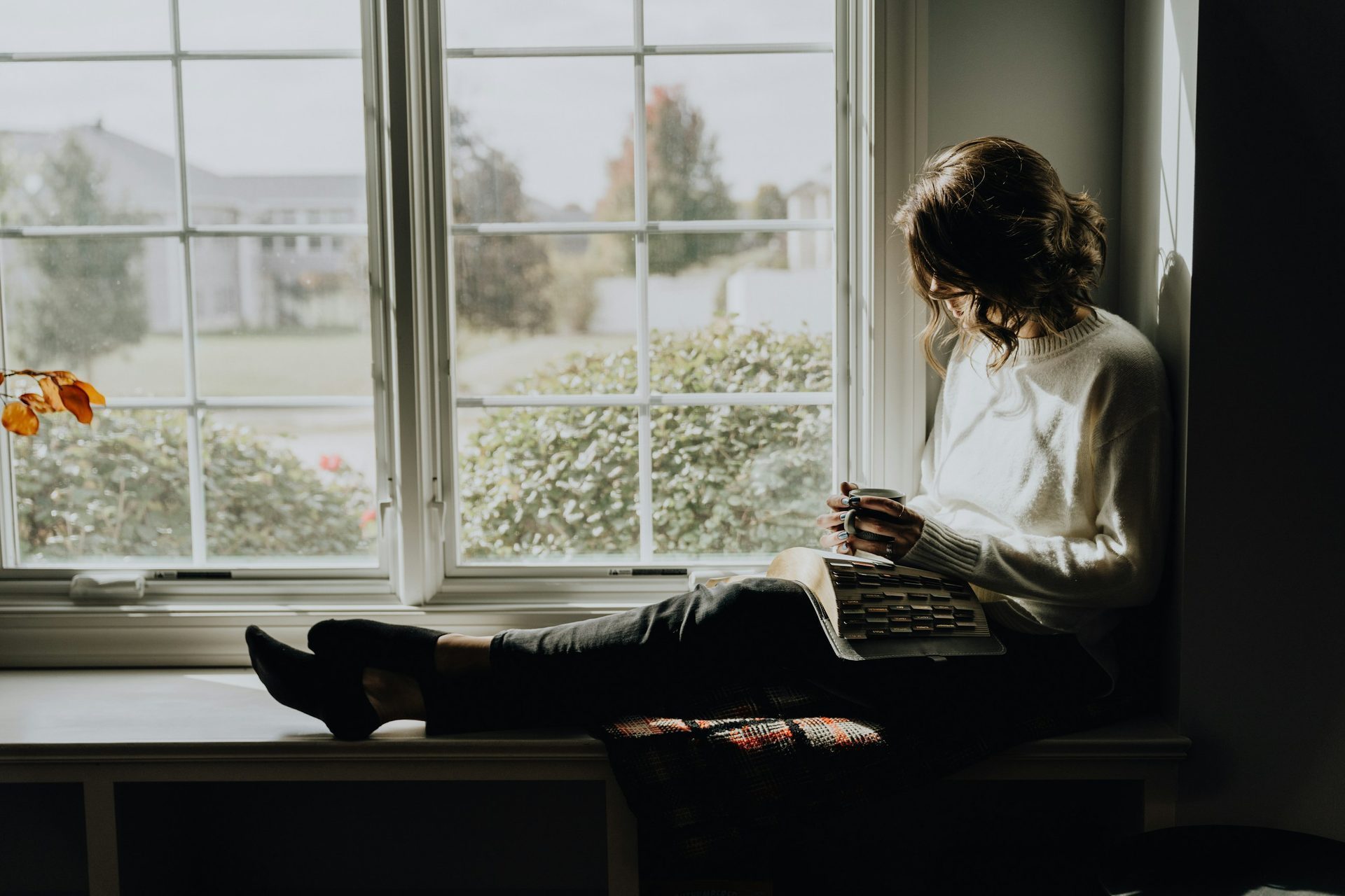 Woman reading in a sunlit window seat, representing calm and ease in everyday life after OCD treatment