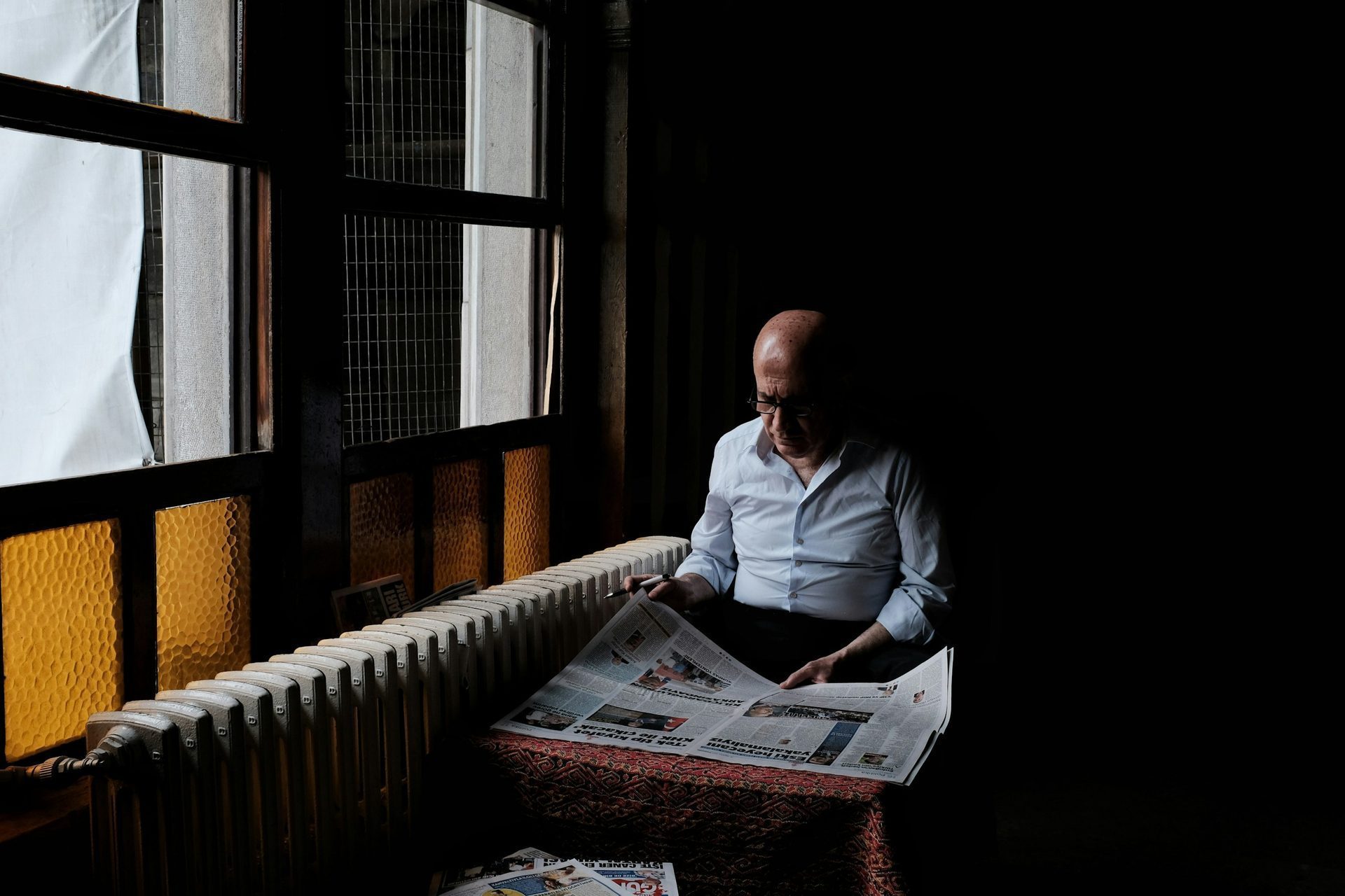 Older man reading the newspaper by a sunlit window, representing rebuilding daily life in opioid addiction treatment