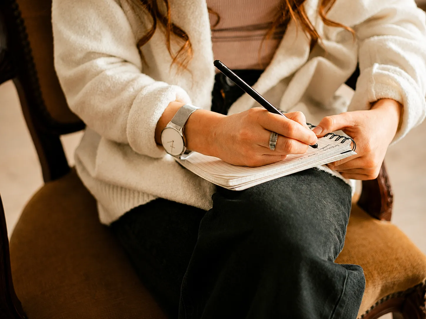 Person writing in a notebook during a therapy session, working on a treatment plan