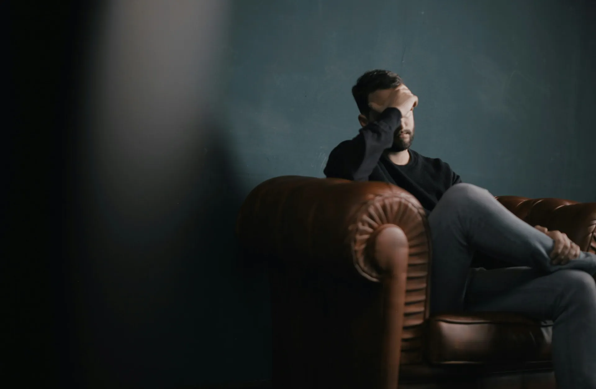 Man sitting alone in a dark room with his head lowered, showing depression and isolation, illustrating trading addiction